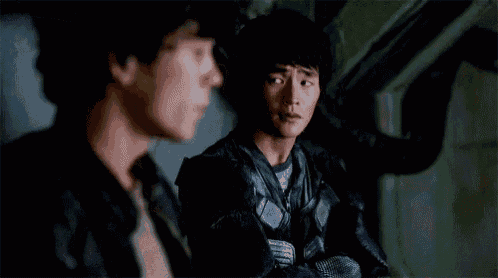 two men are sitting next to each other in a dark room talking to each other .