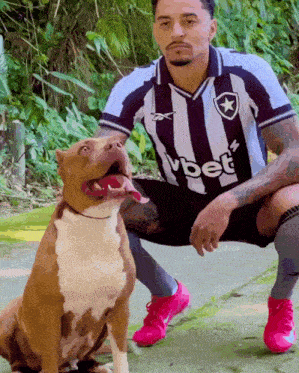 a man wearing a vbet jersey kneeling down next to a dog