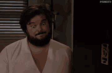 a man with a beard is standing in front of a refrigerator and making a face .