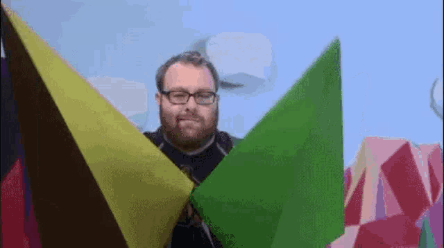 a man with a beard and glasses is holding a green triangle in his hands .