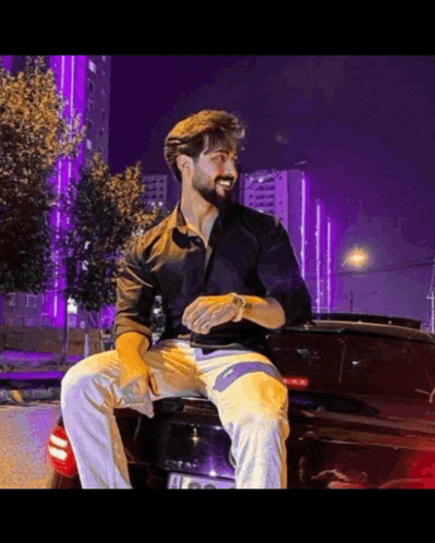 a man in a black shirt sits on the back of a car