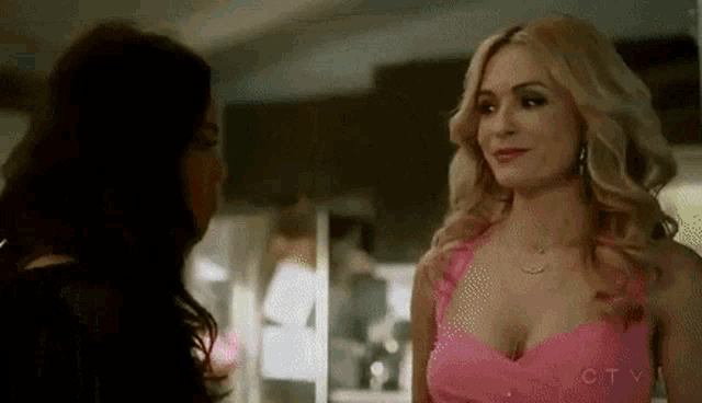 a woman in a pink dress is standing next to another woman in a black dress in a kitchen .