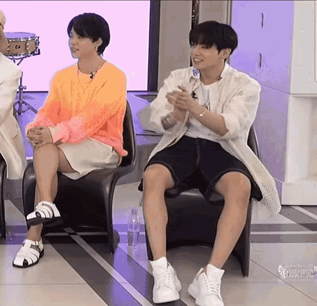 two men are sitting on chairs with their legs crossed