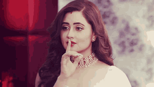a woman holds her finger to her lips while wearing a necklace