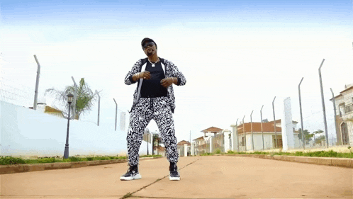 a man in a black and white suit is dancing on a street in front of a fence .