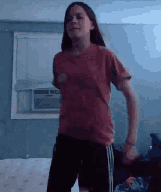 a young girl in a red shirt is dancing in a bedroom .
