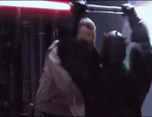 a man in a black mask is holding a red light saber over another man 's head .