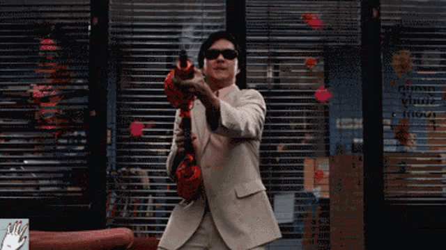 a man in a suit and sunglasses holds a toy gun