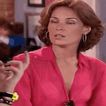 a woman in a pink shirt and hoop earrings is talking to another woman .