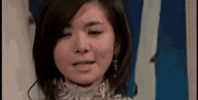 a close up of a woman 's face with a blue and white curtain behind her .