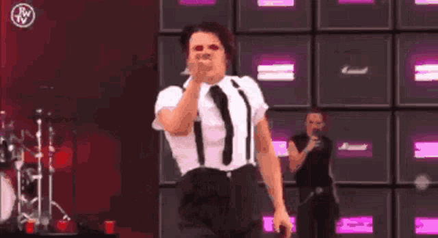 a man in a white shirt and black suspenders is singing into a microphone on stage