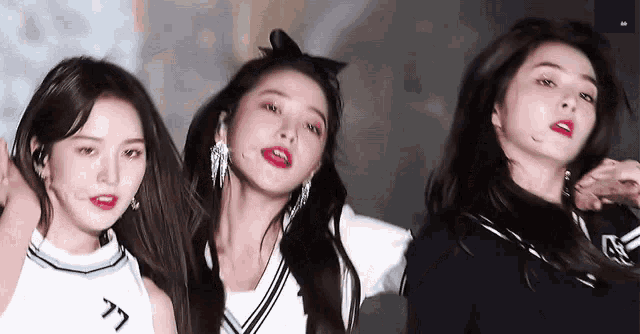 three girls are standing next to each other on a stage and one of them has a bow in her hair .
