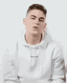 a man in a white hoodie is smiling and laughing while standing in front of a white wall .