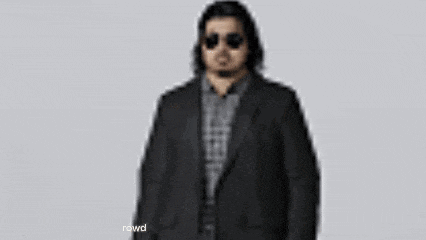 a man wearing sunglasses and a suit is standing in front of a white wall .