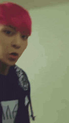 a young man with red hair is standing in front of a wall and making a funny face .