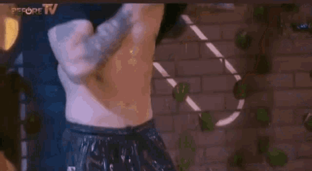 a man without a shirt is standing in front of a brick wall in a gym .