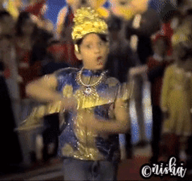 a boy in a blue and gold costume is dancing in front of a crowd with the name misha written on the bottom