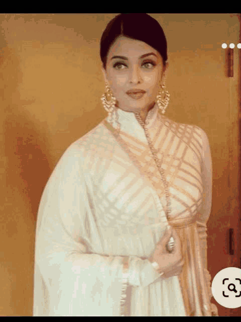 a woman in a white dress and gold earrings stands in front of a door