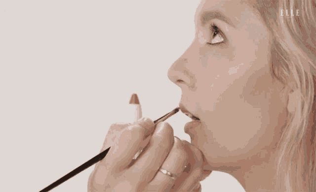 a woman is applying lipstick with a brush to her lips .