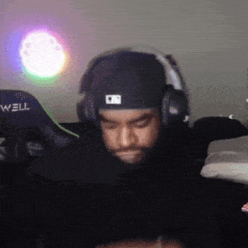 a man wearing headphones and a hat is sitting in front of a well gaming chair .