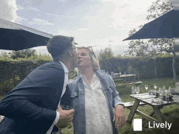 a man in a suit is kissing a woman on the cheek while holding a glass of wine .