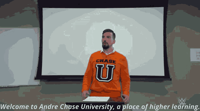 a man wearing an orange chase university shirt stands in front of a white board
