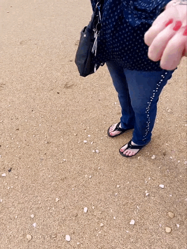 a woman standing on a sandy beach wearing flip flops and jeans