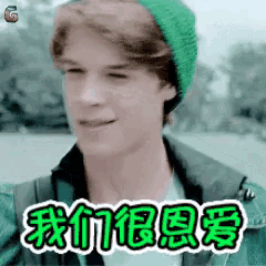 a young man wearing a green hat and a green jacket is making a funny face with chinese writing behind him .