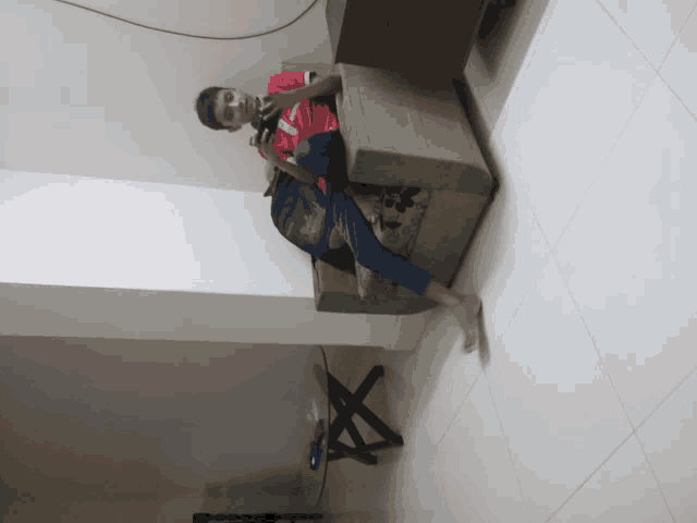 a boy in a red shirt with the letter v on it sits on a couch with his legs crossed