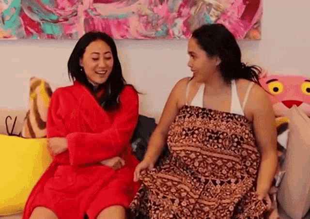 two women are sitting on a couch covered in blankets and talking to each other .