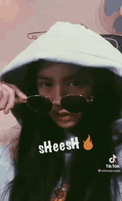 a girl wearing sunglasses and a white hoodie has a tiktok sticker on her face