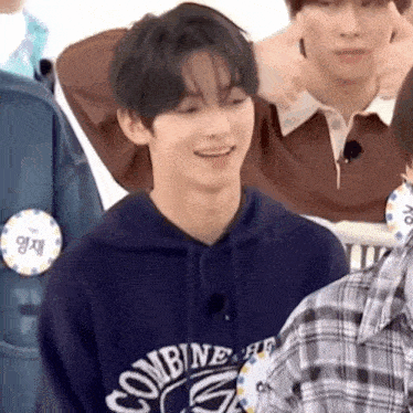 a young man wearing a blue hoodie is smiling while standing next to a group of people .