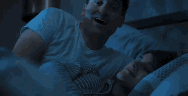 a man is smoking a cigarette while laying next to a woman sleeping in bed .