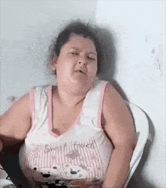 a woman in a pink and white tank top is sitting in a chair and making a funny face .