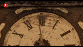 a close up of a clock with roman numerals and the letter b on the bottom right