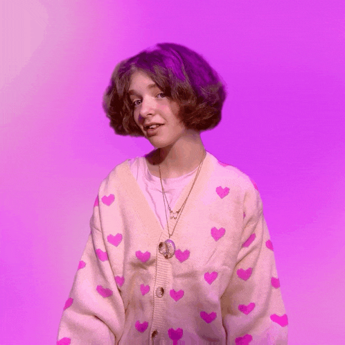 a girl with purple hair is wearing a pink cardigan with pink hearts on it