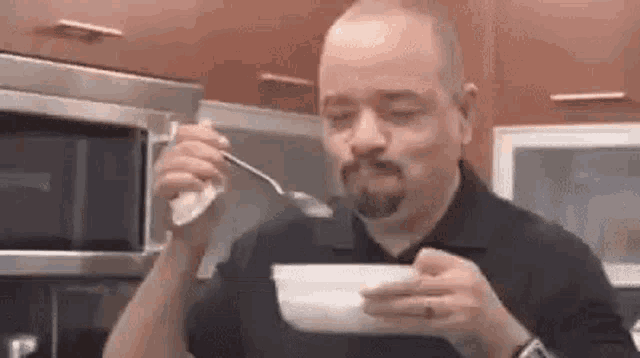 a man is eating a bowl of cereal with a spoon in his mouth .