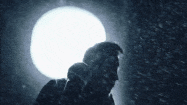 a man is singing into a microphone in the rain in front of a white light .