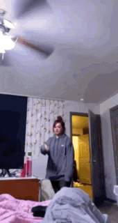 a girl is dancing in a bedroom with a ceiling fan .