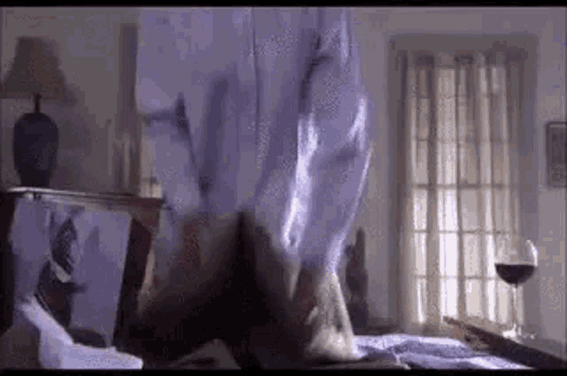 a man in a white shirt is standing on a bed in a bedroom .