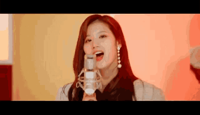 a woman is singing into a microphone in front of a red background .