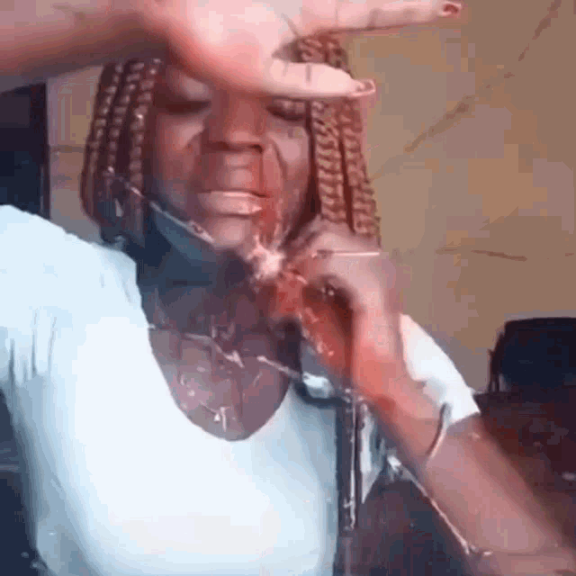 a woman with braids is covering her face with her hand while holding a bottle of water .