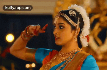 a woman in a blue and gold dress is dancing a traditional dance .