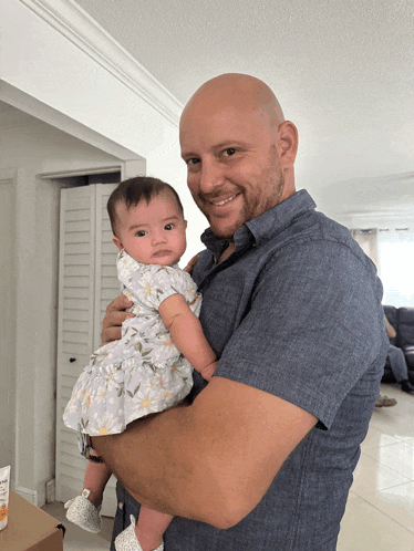 a man is holding a baby in his arms and the baby is wearing a floral dress