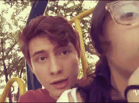 a man and a woman are sitting on a swing set and the man is wearing glasses