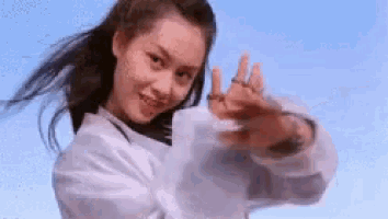 a woman in a white shirt is standing in front of a blue sky with her hands outstretched .