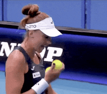 a woman wearing a visor that says azto on it is holding a tennis ball