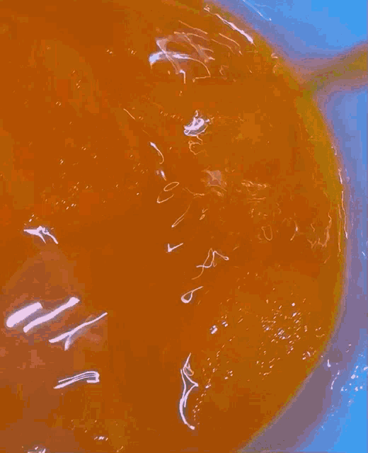 a close up of a bowl of orange liquid with a yellow spoon in it