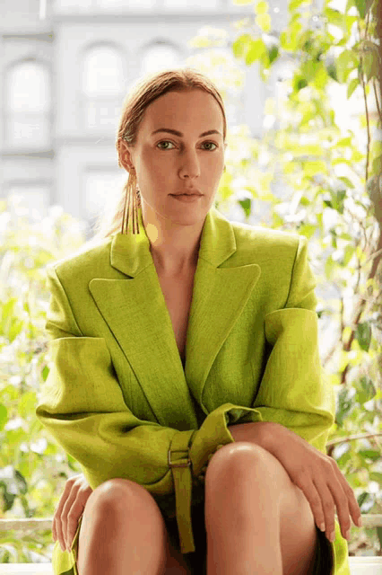 a woman in a bright green jacket is sitting on a window sill