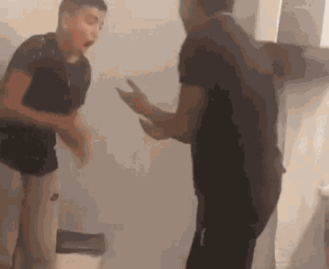two men are standing next to each other in a room . one of the men is holding a cell phone .